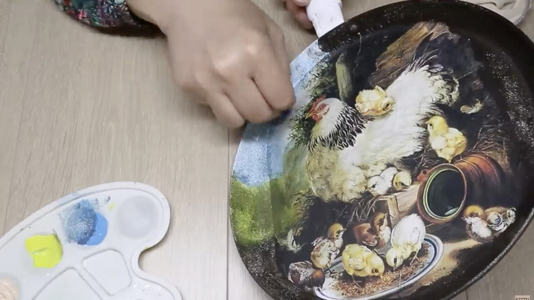 A person adding finishing details to a decoupaged frying pan.