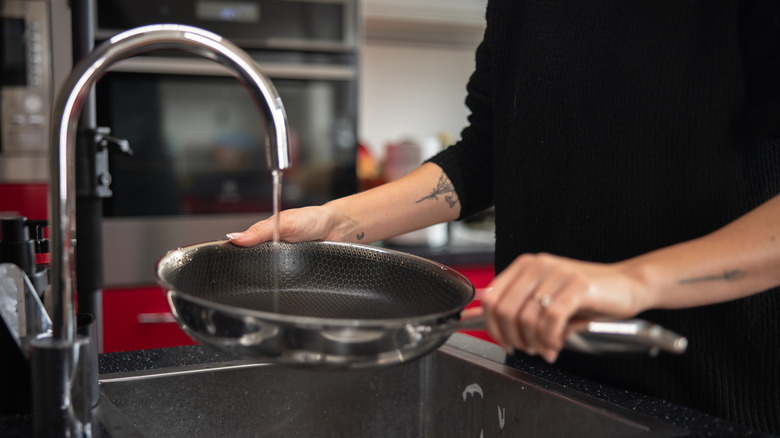 A person holds a frypan under a running faucet in the kitchen.