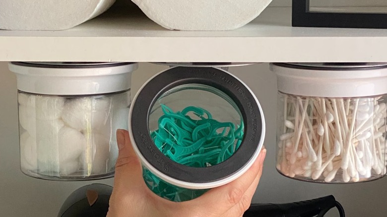 Someone holding a magnetic glass jar with floss sticks