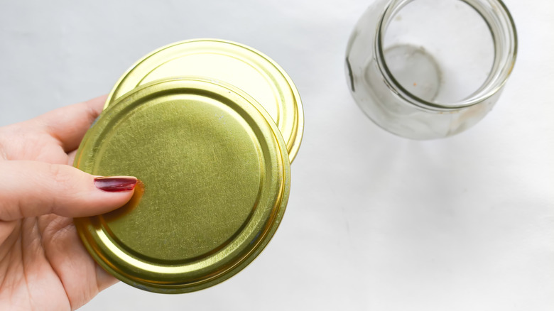 Woman's hand holding old jar lids with empty jar in the background.