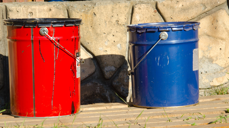 Red and blue buckets sitting on a wood pallet outdoors.