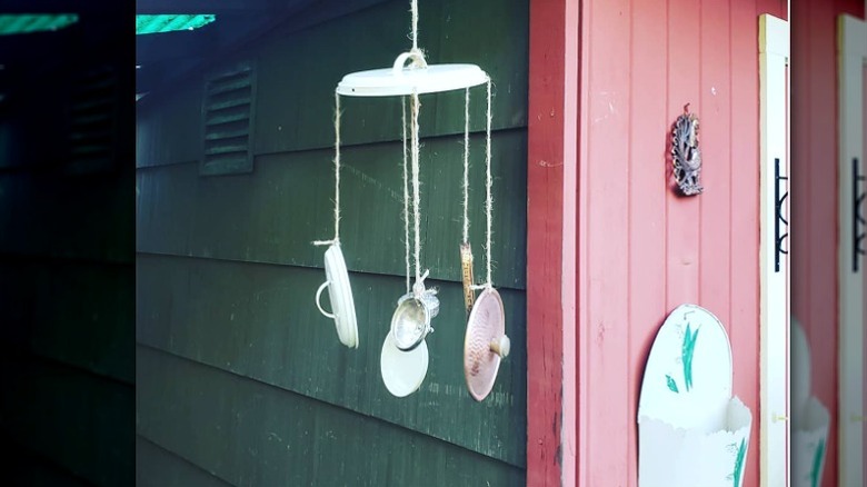 A rustic DIY wind chime created out of pot lids hangs beside a red front door.