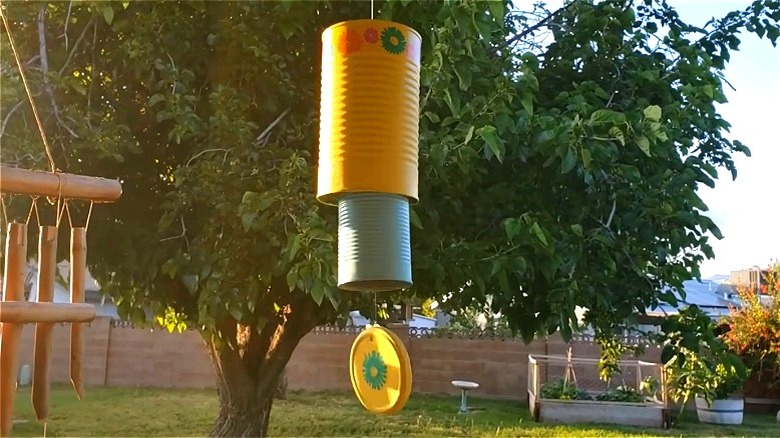 A colorful wind chime made from repurposed tin cans hanging in a sunny garden.