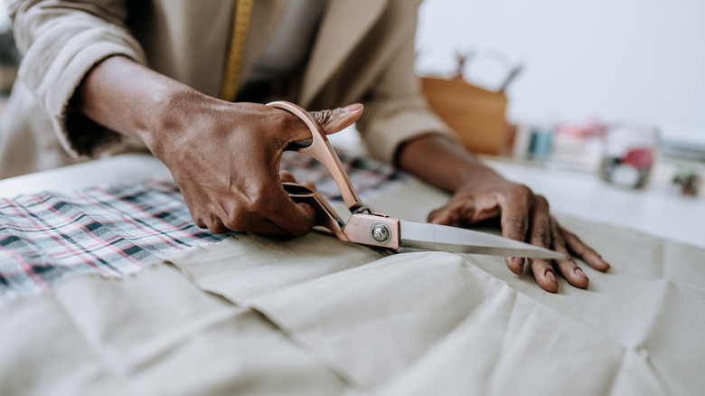 A person's hands holding and cutting fabric with large scissors.