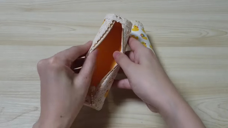 A person's hands holding a storage pouch made from a toilet paper tube and fabric.