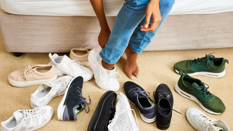 person putting shoes on with a messy pile of shoes around them