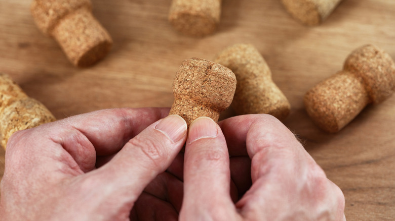 Hands holding a champagne cork over a table with more corks on it