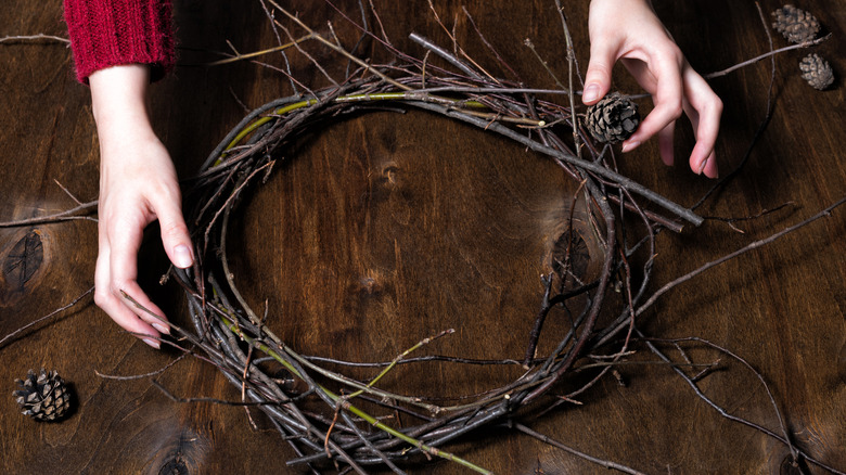 Hands holding a rustic grapevine wreath and pine cones.