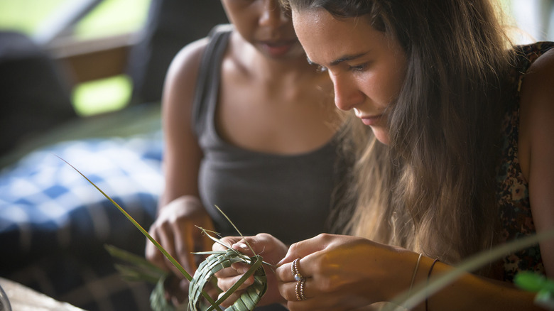 Two women folding palm fronds.