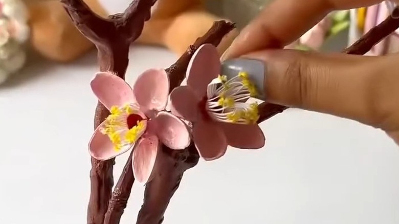 Fingers gluing a cherry blossom flower on a brown stem