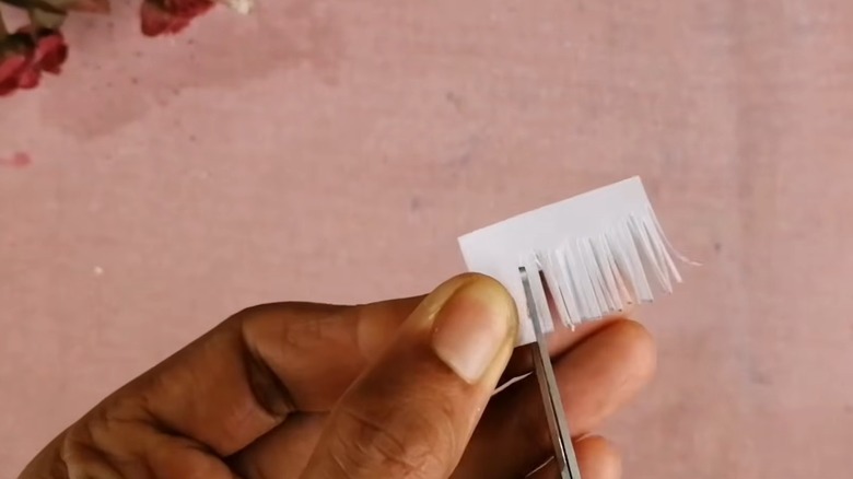 Hands cutting fringes on one side of a white strip