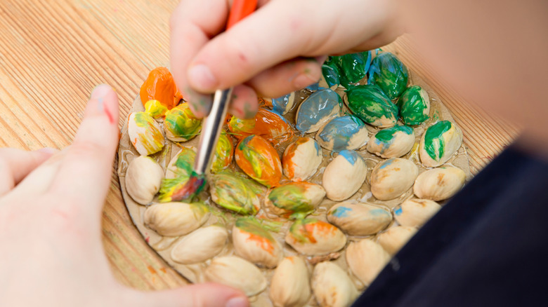 Hands coloring pistachio shells glued to a cardboard piece
