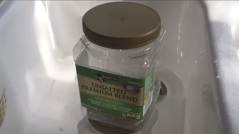 An empty plastic container of unsalted nuts with a large gold lid in a kitchen sink.