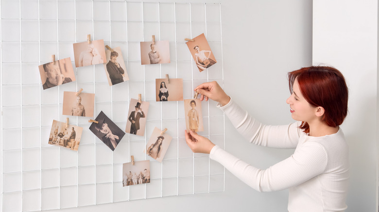 Woman hanging photos on a wall grid.