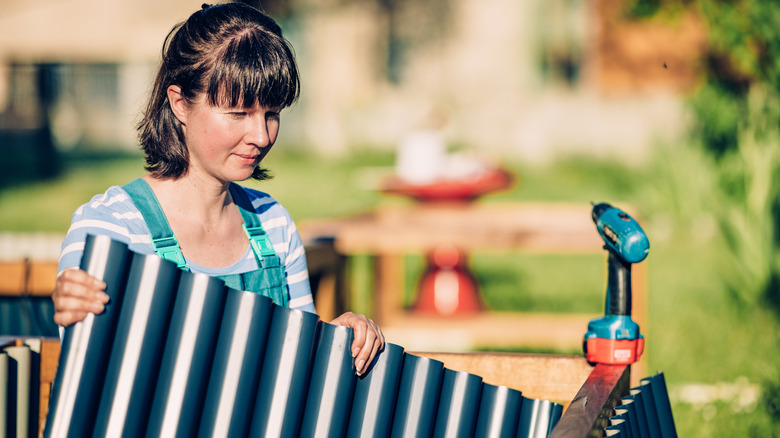 A woman holding a sheet of corrugated metal preparing to build.