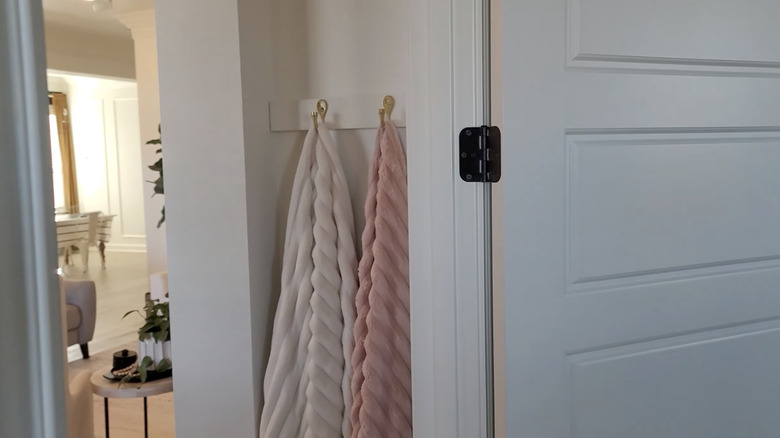 Blankets hanging from hooks in the nook of a hallway by a white door