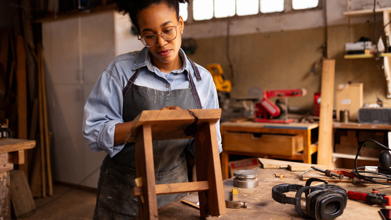 A woman making a stool in a garage with a woodworking bench and tools