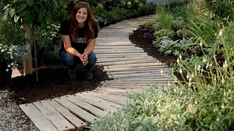 A gardener squatting down next to a completed pathway made from pallet wood