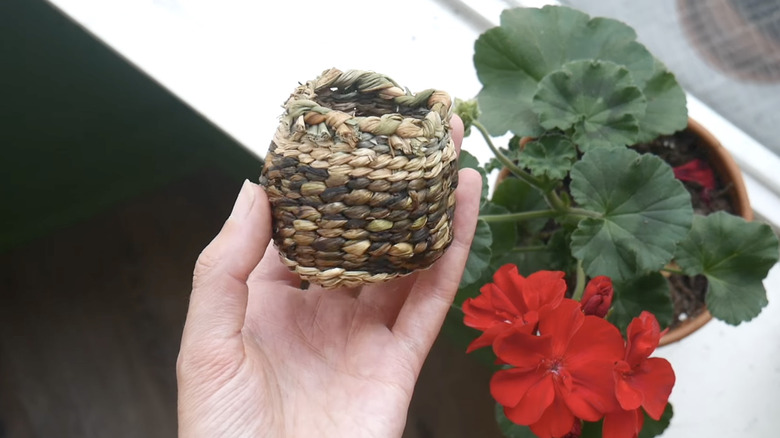 A person holds a mini basket woven using dandelion stems