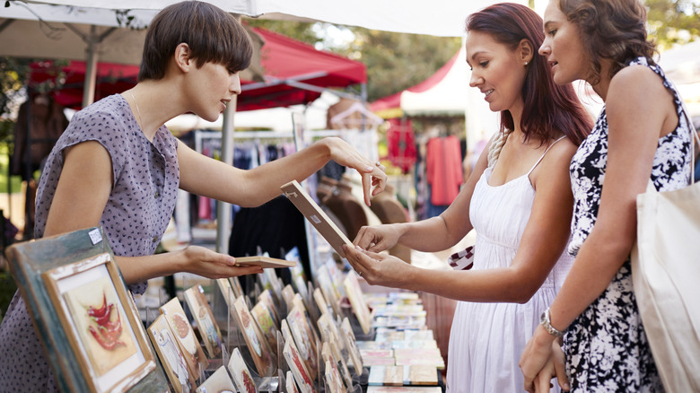 woman and her friend discussing art being sold in an outdoor market setting