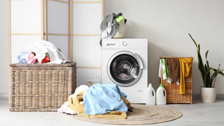 Untidy laundry room with piles of dirty clothes on the floor and hanging out the hamper