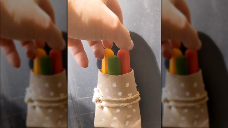 A hand takes a marker from a wall-mounted storage pocket made from an empty toilet paper roll.