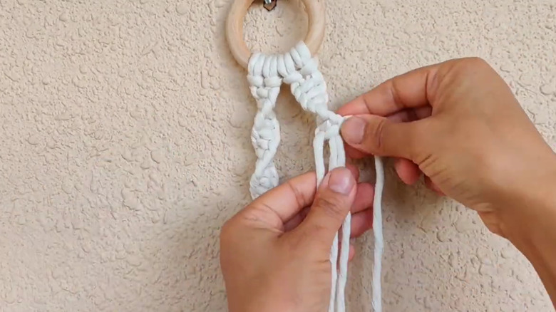 A close-up of a person weaving macramé rope onto a wooden ring