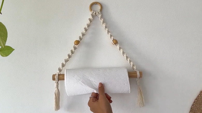 A DIY macramé paper towel holder on a white wall