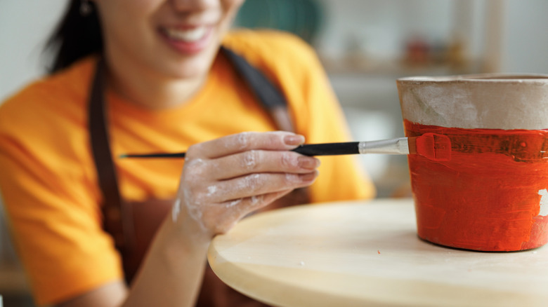 A person paints a terracotta pot bright orange and white