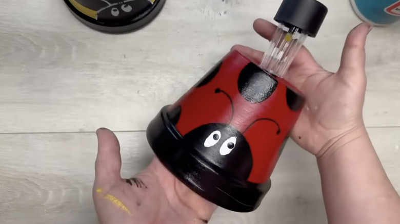Two hands hold an upside down terracotta pot painted to look like a ladybug with a solar light fitted in the drainage hole.