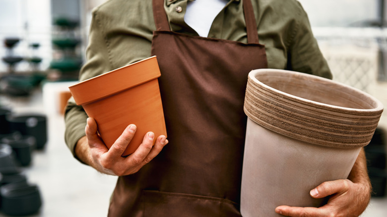 A person wearing a brown apron holds a large and small terracotta pot in their hands.