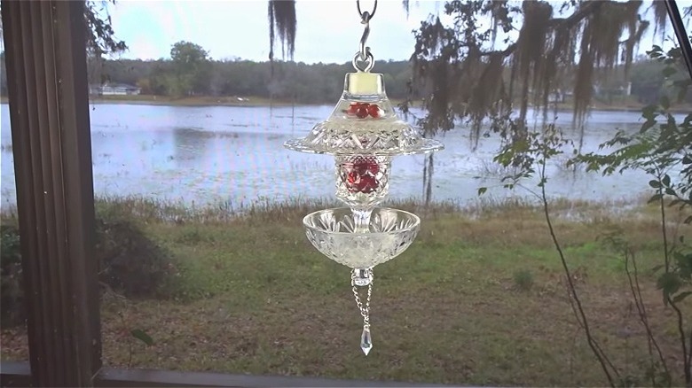 Birdfeeder made from vintage glass dishes hanging outside a window with a view of the lake.
