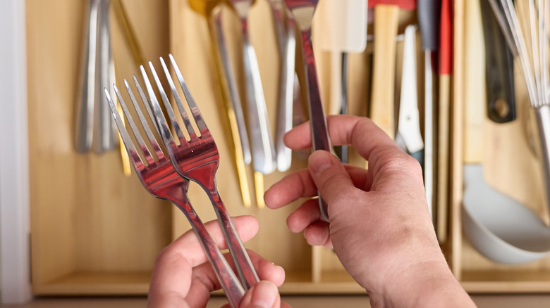 Person holding forks over a drawer