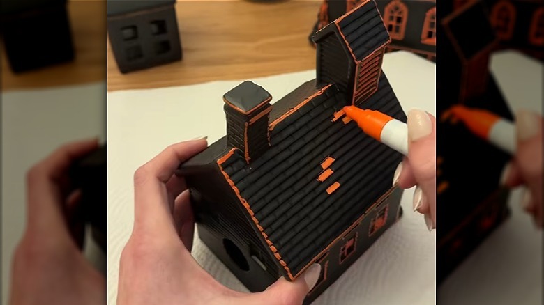 A person using a sharpie to turn a small house into a spooky Halloween one using an orange sharpie