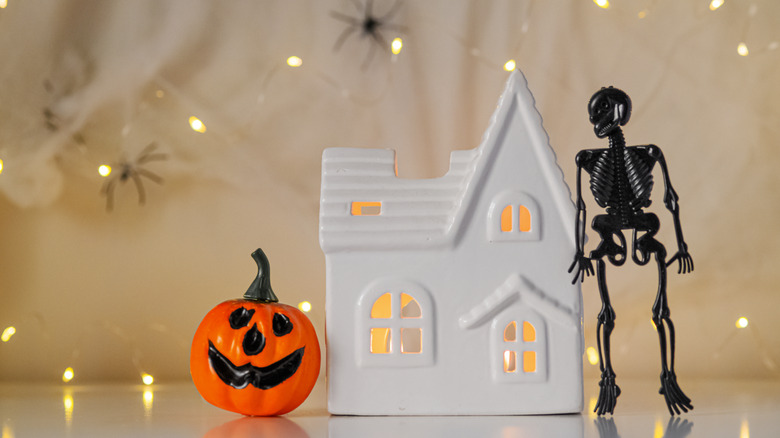 A Halloween display with a small home, jack-o-lantern and skeleton