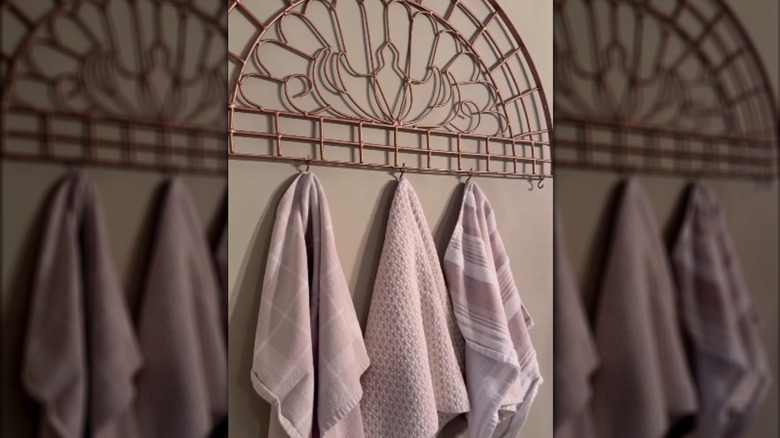 Rose gold-colored metal wall art with hooks holding towels