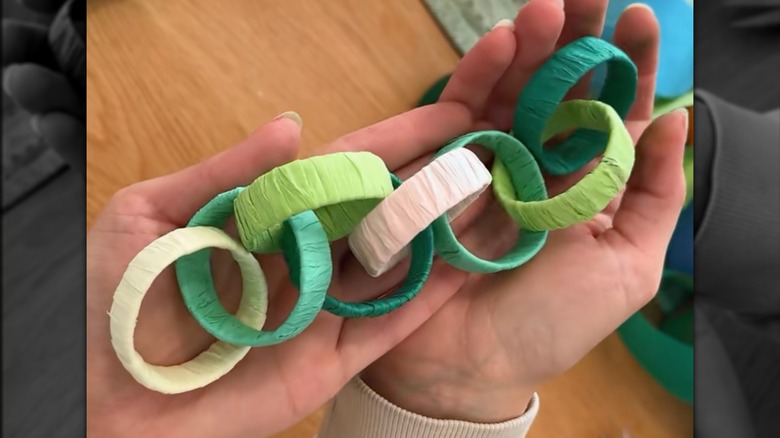 Two hands hold a green and cream chain garland made from toilet paper rolls and colored paper.