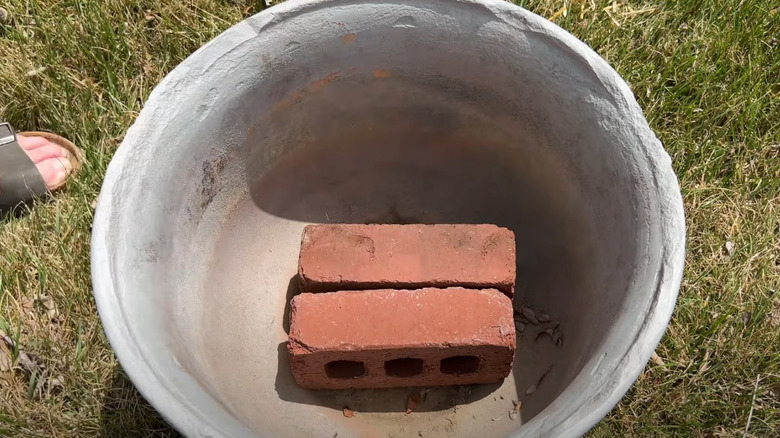 Two red bricks at the bottom of a large planter.
