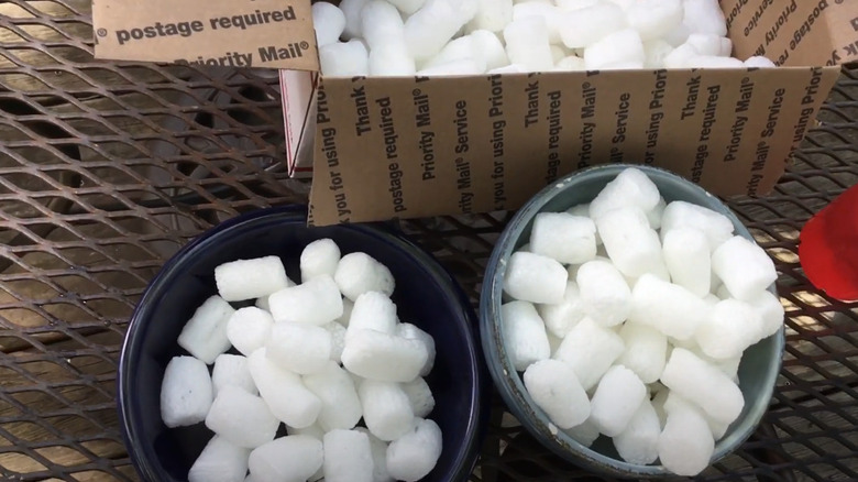 Two small pots filled with white packing peanuts sitting next to a U.S. postal service box.