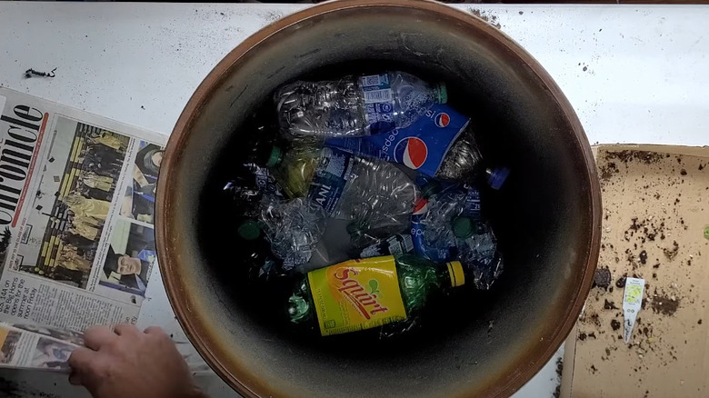 A series of crushed plastic bottles at the bottom of a large potted planter.