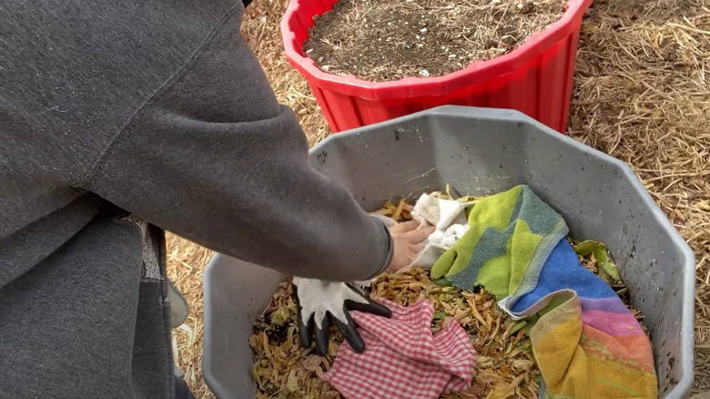 A woman pushing down rags on top of yard waste in a planter.