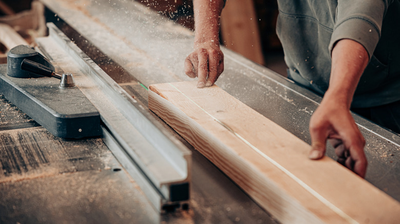 A carpenter guides a wooden plank through a table saw.