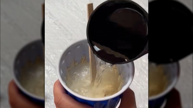 A hand pours water into a cup of flour to make papier mache paste.