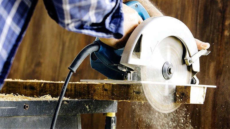 Close-up of a person cutting wood piece in a workshop garage