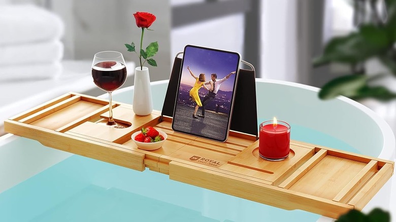The Royal Craft Wood bathtub tray across a bathtub with a bowl of strawberries, a rose, a glass of wine, and a lit candle on top.