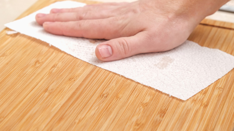 A hand holding a paper towel wiping down a bamboo or wooden board.