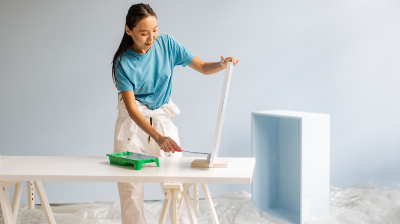 A person painting the components of a small bookcase