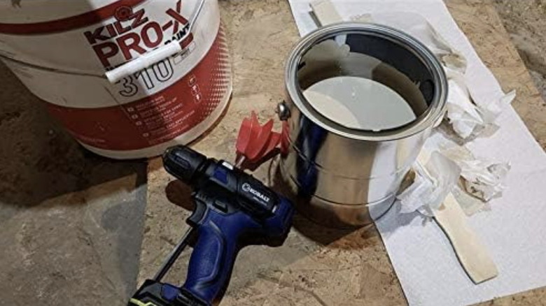 The Edward Tools paint mixer attachment, a drill, a can of paint, paper towels, and a large bucket on the ground
