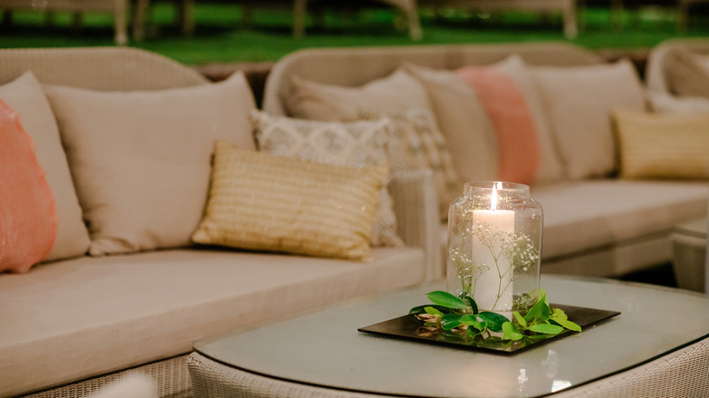Warm beige colored outdoor seating with soft cushions, a table decorated with a candle and green leaves