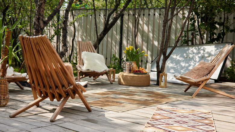 A cozy patio with curved wooden chairs, fluffy pillows, and pattern rugs